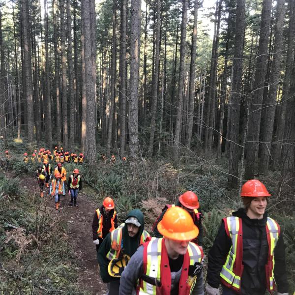 Students wearing safety gear hiking up a forest path.